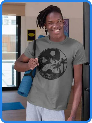 A black man wearing a gray unisex t-shirt with a yin yang summer moon design. The man is carrying a yoga mat over his shoulder. The t-shirt is a fun and positive way to express your love of yoga and the yin yang symbol.